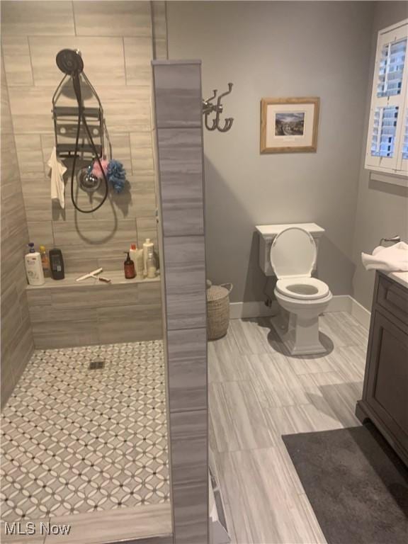 full bath with baseboards, toilet, vanity, and a tile shower