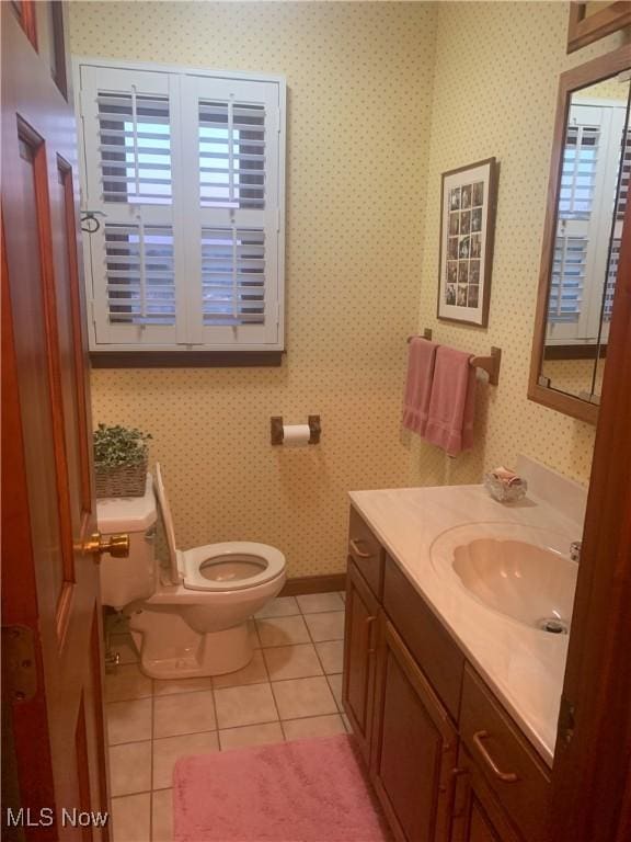 half bath with tile patterned flooring, toilet, wallpapered walls, and vanity