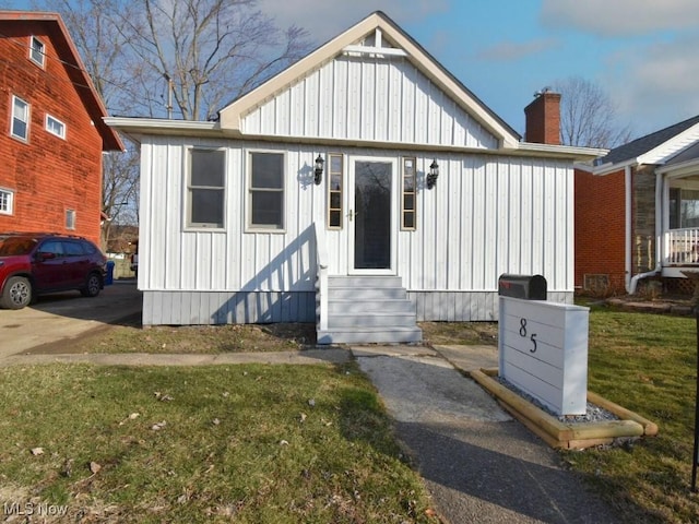 bungalow-style home featuring a chimney, entry steps, a front yard, and board and batten siding