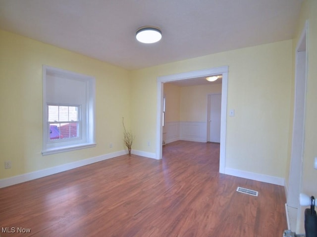 empty room with wood finished floors, visible vents, and baseboards