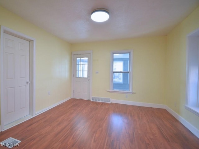 empty room featuring wood finished floors, visible vents, and baseboards