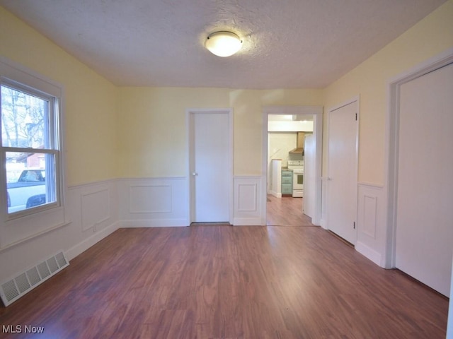 empty room with wainscoting, wood finished floors, visible vents, and a textured ceiling