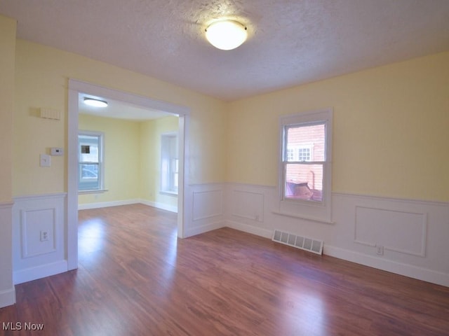 unfurnished room featuring visible vents, wainscoting, a textured ceiling, and dark wood-style flooring