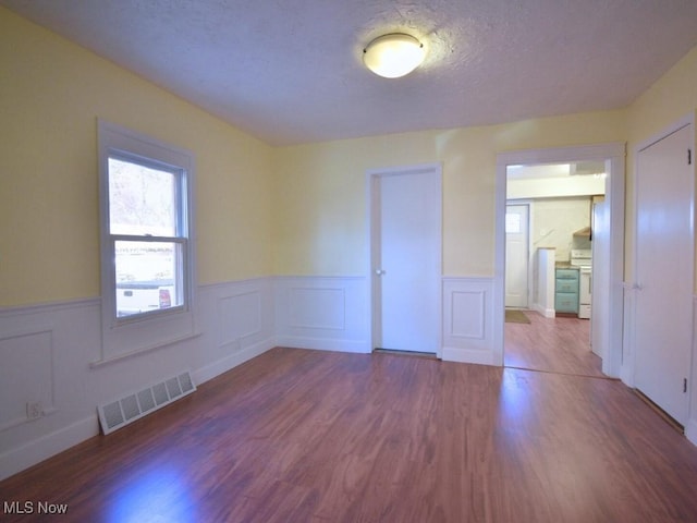 unfurnished room with visible vents, a textured ceiling, wood finished floors, and wainscoting