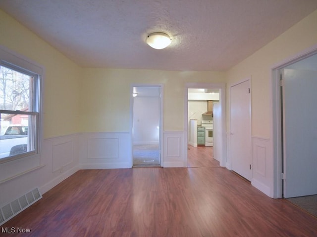 spare room with wainscoting, wood finished floors, visible vents, and a textured ceiling