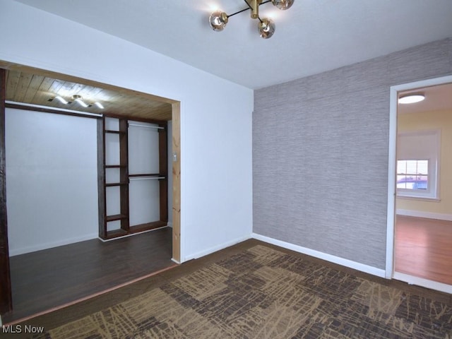 unfurnished room with baseboards, wood finished floors, an accent wall, and wallpapered walls