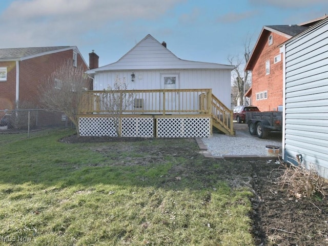 rear view of property featuring a lawn, a wooden deck, and fence