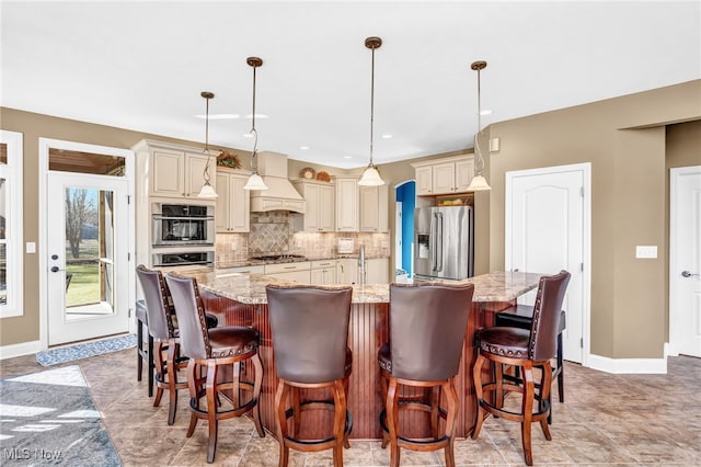 kitchen with premium range hood, tasteful backsplash, cream cabinets, appliances with stainless steel finishes, and light stone countertops