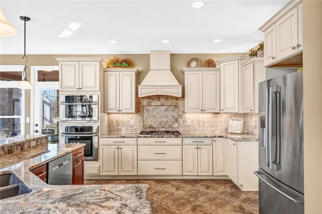 kitchen with custom range hood, light stone countertops, tasteful backsplash, and appliances with stainless steel finishes