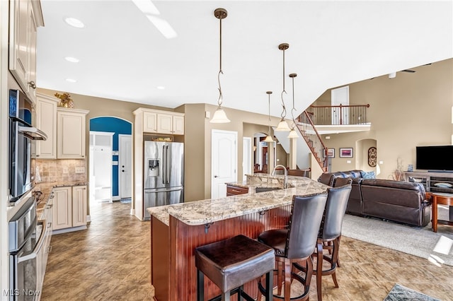 kitchen with stainless steel refrigerator with ice dispenser, a sink, tasteful backsplash, open floor plan, and arched walkways