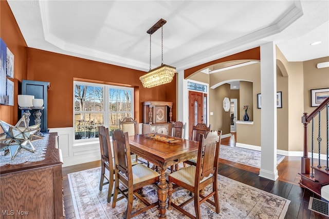 dining space with stairway, a wainscoted wall, arched walkways, dark wood-style flooring, and a raised ceiling