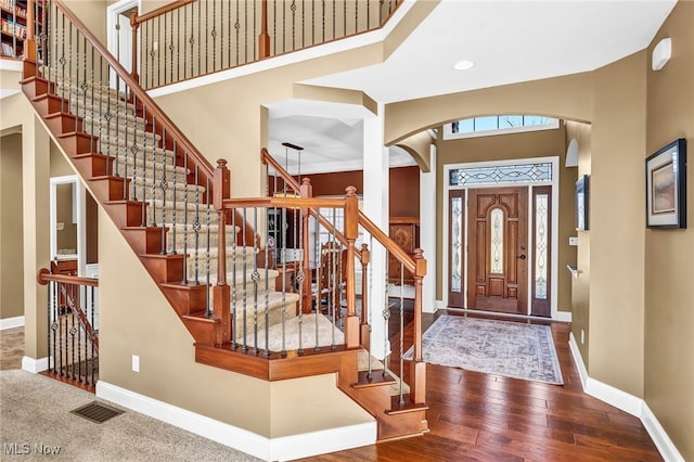 foyer entrance featuring visible vents, baseboards, a high ceiling, arched walkways, and wood-type flooring