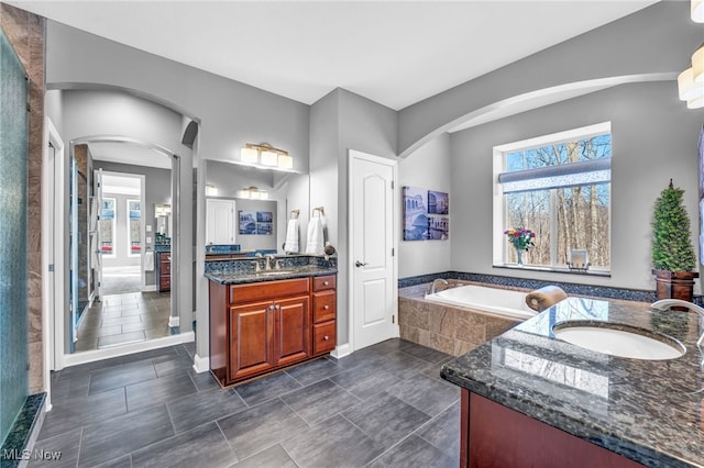 bathroom with two vanities, a garden tub, and a sink