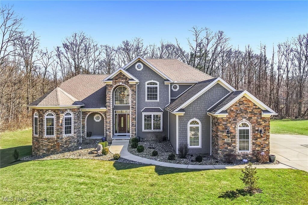 view of front of property featuring stone siding, roof with shingles, and a front yard