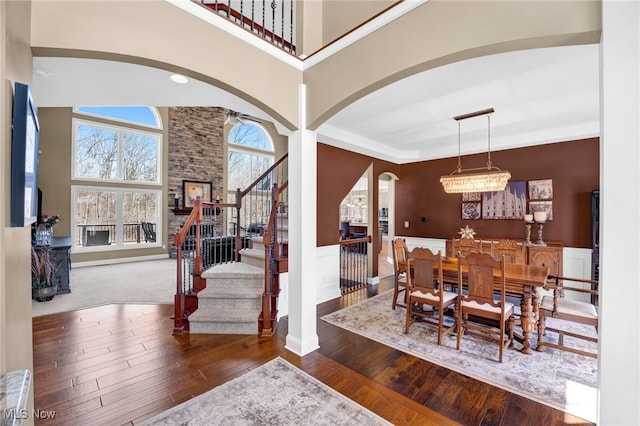 dining room with stairway, a high ceiling, wood-type flooring, wainscoting, and crown molding