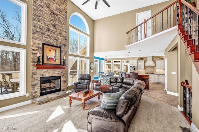 living area featuring baseboards, visible vents, ceiling fan, a stone fireplace, and light colored carpet