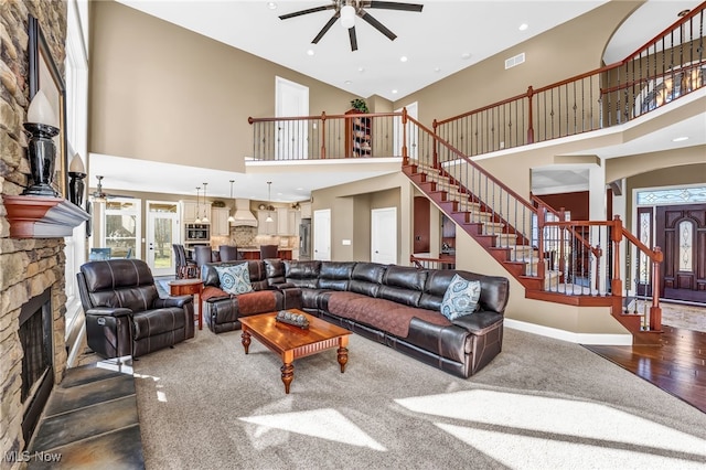 living area featuring visible vents, a fireplace, ceiling fan, stairs, and a towering ceiling