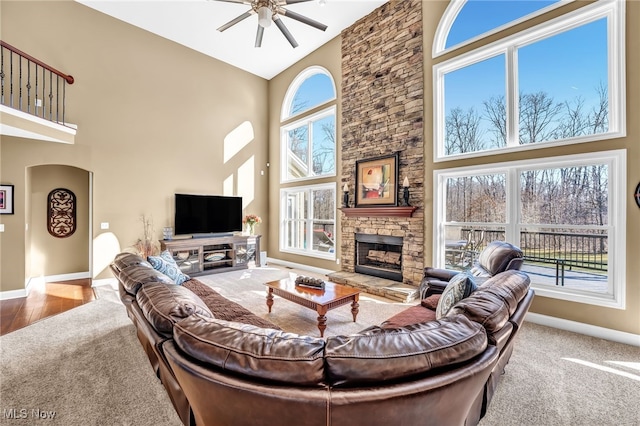 living room with baseboards, a high ceiling, a stone fireplace, and carpet flooring