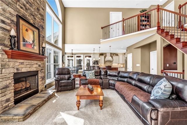 carpeted living area featuring a stone fireplace, a towering ceiling, and stairs