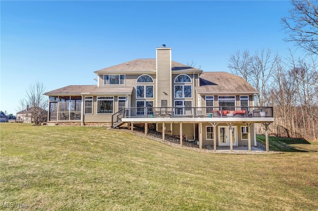 back of property with a patio, a wooden deck, a sunroom, a chimney, and a lawn