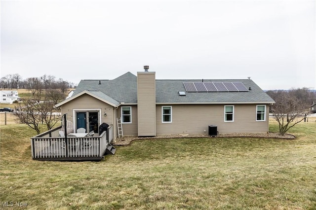 rear view of house featuring cooling unit, solar panels, a yard, a chimney, and a deck