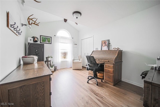 office space featuring baseboards, vaulted ceiling, and light wood finished floors