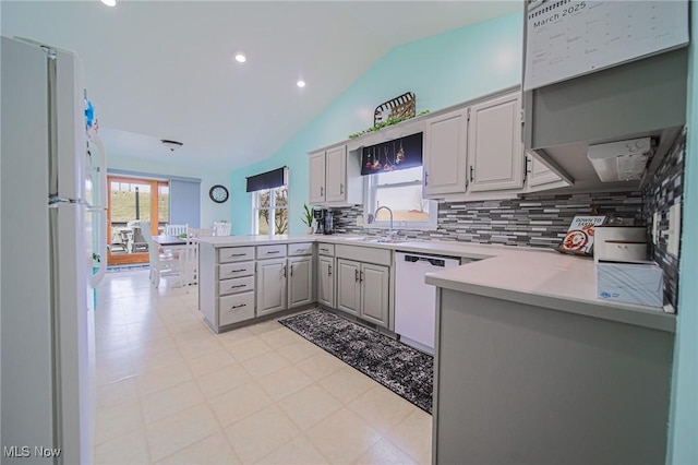 kitchen with light countertops, lofted ceiling, a peninsula, white appliances, and a sink