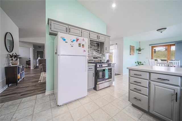 kitchen featuring backsplash, gray cabinetry, light countertops, freestanding refrigerator, and stainless steel gas stove