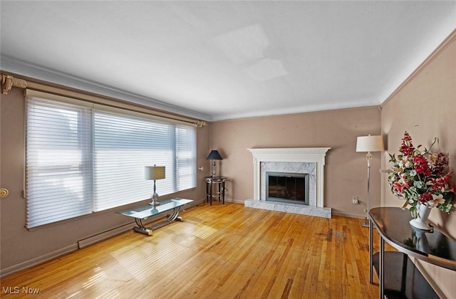 living area with a high end fireplace, crown molding, baseboards, and light wood finished floors