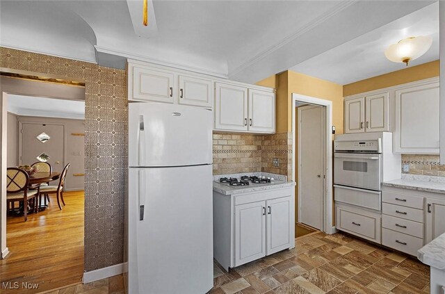 kitchen with a warming drawer, white appliances, tasteful backsplash, and white cabinetry