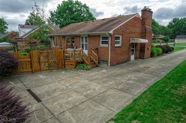 back of house featuring brick siding, fence, a wooden deck, a chimney, and a patio area