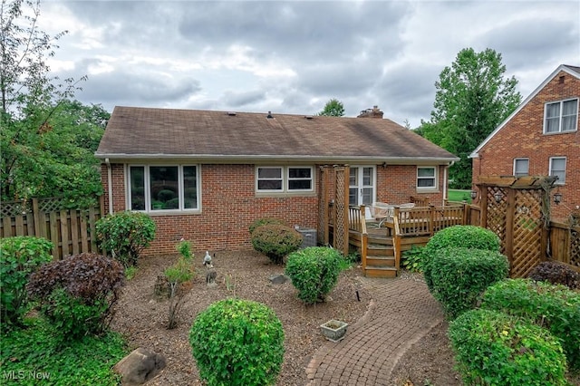 rear view of house featuring a shingled roof, fence, brick siding, and a wooden deck