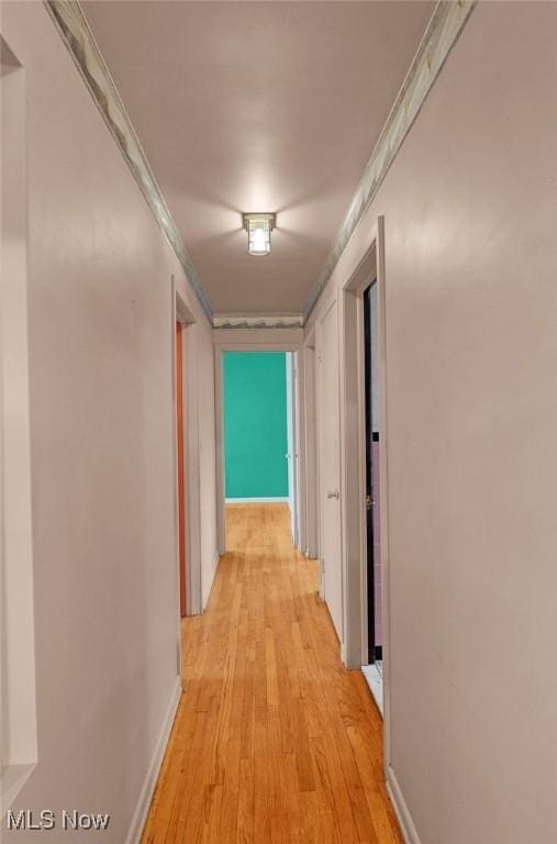 hallway featuring baseboards, light wood-style flooring, and crown molding