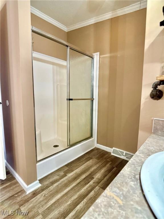 full bath featuring visible vents, wood finished floors, a shower stall, crown molding, and baseboards