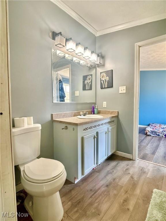 half bath with baseboards, toilet, ornamental molding, wood finished floors, and vanity