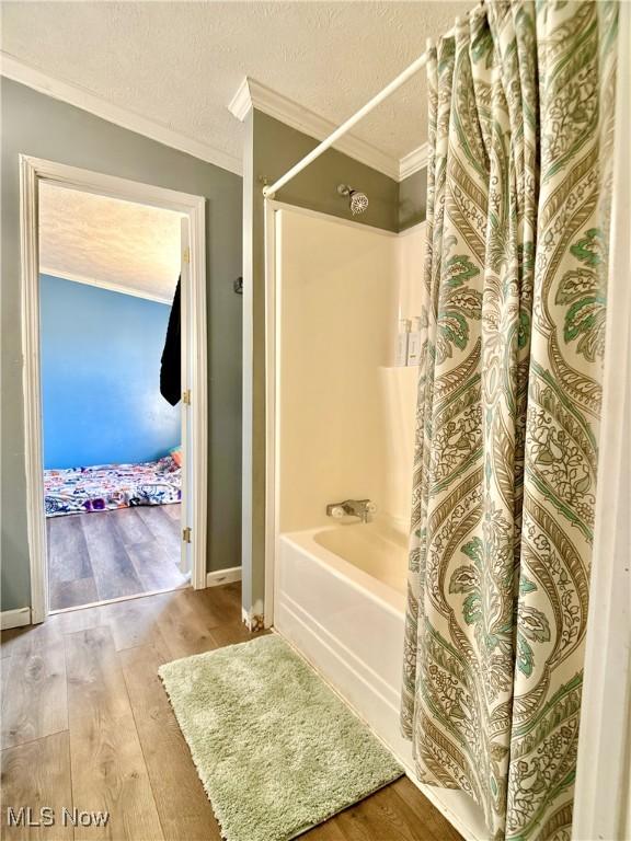 bathroom featuring crown molding, a textured ceiling, shower / tub combo with curtain, and wood finished floors