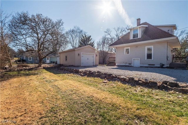 rear view of property with an outbuilding, a lawn, a detached garage, a shingled roof, and a chimney