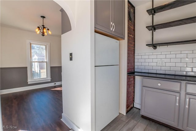 kitchen featuring wood finished floors, a wainscoted wall, arched walkways, freestanding refrigerator, and dark countertops