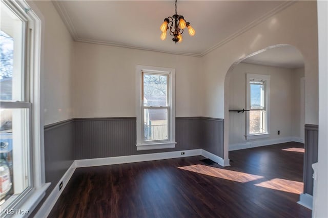 unfurnished room featuring wood finished floors, arched walkways, a wealth of natural light, and wainscoting