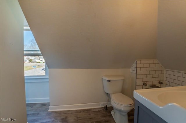 bathroom with toilet, lofted ceiling, wood finished floors, baseboards, and vanity