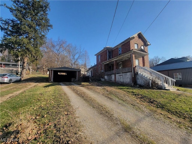 view of front facade with brick siding, dirt driveway, a front yard, a carport, and an outbuilding