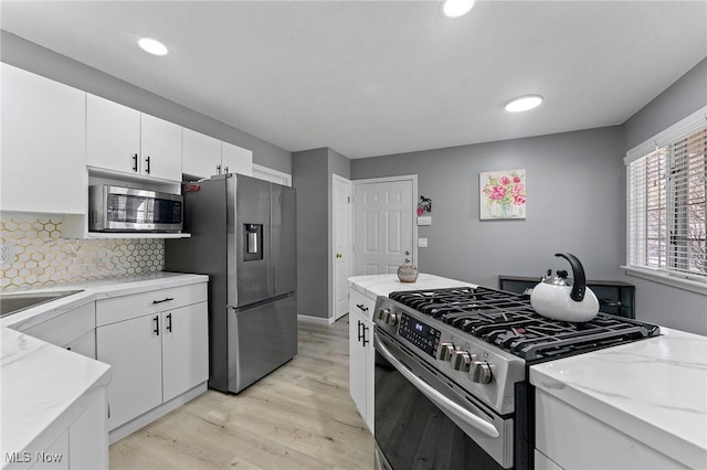 kitchen with stainless steel appliances, white cabinets, decorative backsplash, and light wood-style flooring