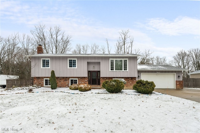 bi-level home with fence, driveway, a chimney, a garage, and brick siding