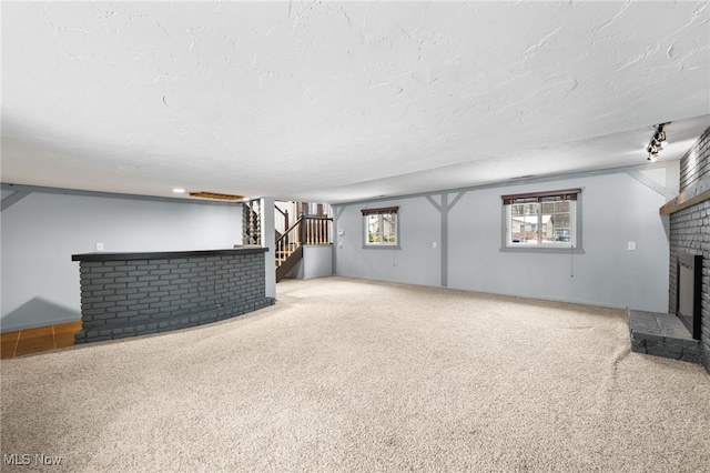 unfurnished living room featuring a wealth of natural light, stairway, a textured ceiling, and a fireplace