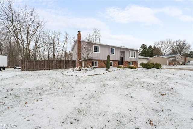 raised ranch with brick siding, an attached garage, a chimney, and fence