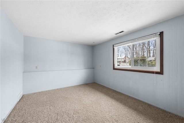 carpeted spare room with visible vents and a textured ceiling