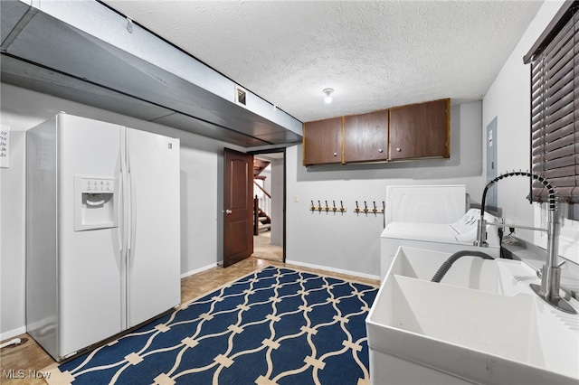 washroom with washing machine and dryer, cabinet space, a textured ceiling, and baseboards