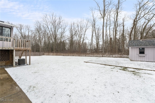 snowy yard featuring central AC, a fenced backyard, a storage shed, an outdoor structure, and a wooden deck