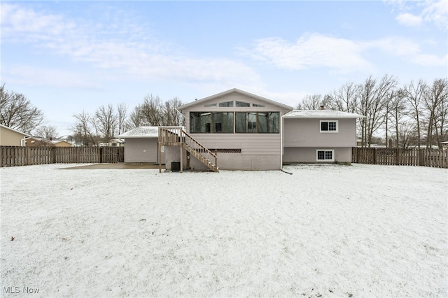 snow covered rear of property with stairway, a fenced backyard, and a sunroom