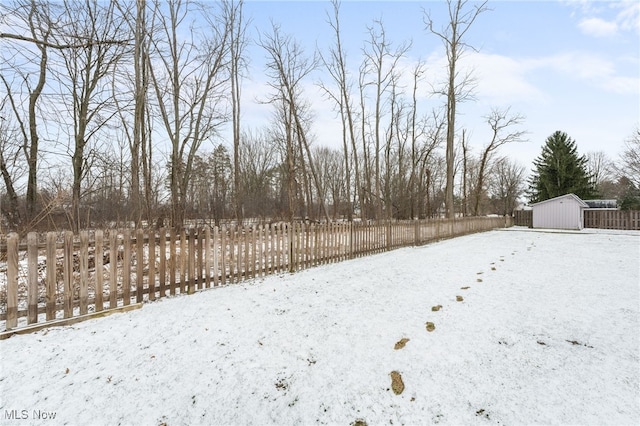 snowy yard featuring a storage shed, an outdoor structure, and fence private yard